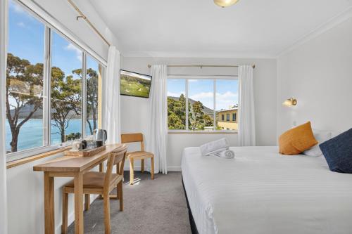 a white bedroom with a bed and a table and windows at Lufra Beachside Hotel in Eaglehawk Neck