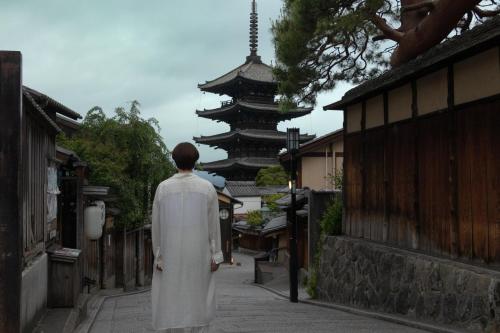 a man in a white robe walking down a street with a pagoda at Sowaka in Kyoto
