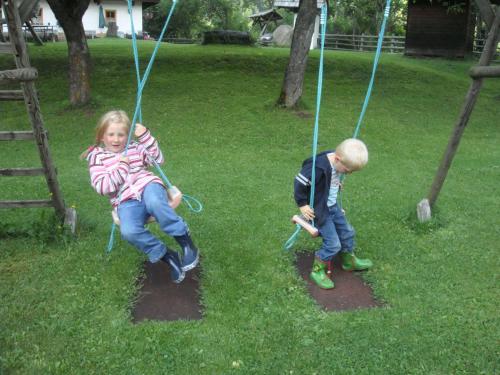 two children playing on a swing in a yard at Ferienwohnung Lahnerhof in Arriach