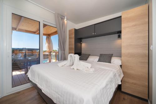 a bedroom with a bed with white sheets and a balcony at Camping Nevia - Mobile Homes with Heated Private Pool in Neviđane