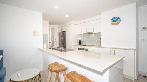 a white kitchen with a counter and two stools at Whispering Waves On Boyd in Woorim