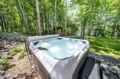 a hot tub in a field with trees in the background at Chalet Mid-Century - Lakeside Joseph - Le Charlo in Saint-Pierre-Baptiste