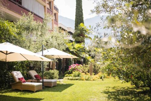 a garden with umbrellas and chairs on the grass at Hotel Gartenresidence Zea Curtis in Merano