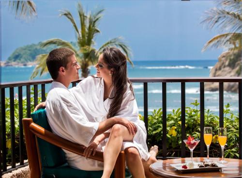 a man and woman sitting at a table with the ocean in the background at Barceló Huatulco - All Inclusive in Santa Cruz Huatulco