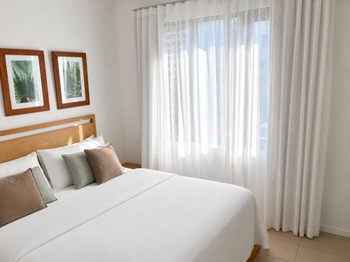 a bedroom with a large white bed and a window at Azuri Appartement De Luxe & Pool in Roches Noires