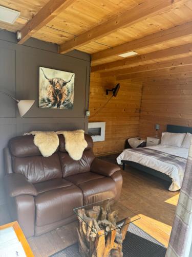 a living room with a leather couch and a bed at Star Gazer Cabin in Inversnaid