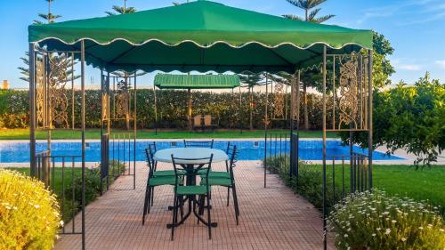 a table and chairs under a green umbrella next to a pool at Charming Villa in Tou Ganaou with Private Pool in Ti nʼ Saïd