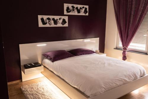 a bedroom with a white bed with purple pillows at Appartement confortable à Apach avec balcon in Apach