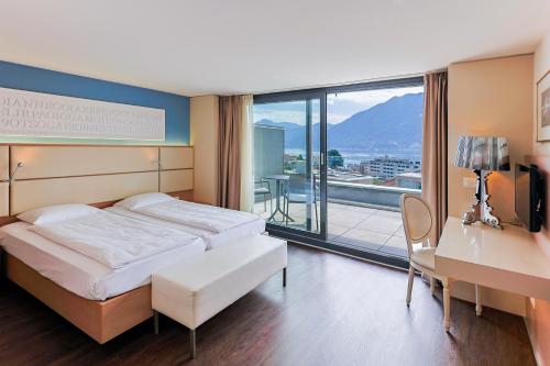 a bedroom with a bed and a desk and a balcony at Hotel Muralto Locarno in Locarno