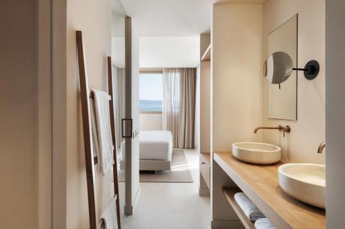 a hotel bathroom with two sinks and a bedroom at Sabatic Formentera Autograph Collection in Es Pujols