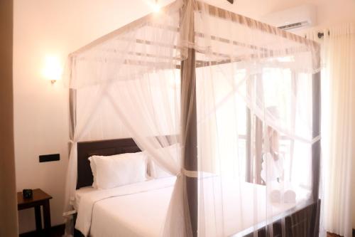 a bedroom with a canopy bed with a window at Parrot Perch Villa Dickwella in Dickwella