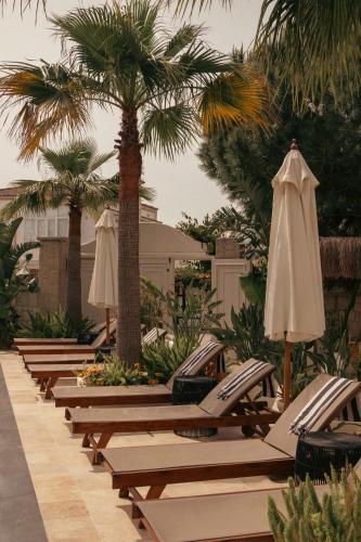 eine Reihe von Liegestühlen mit Sonnenschirmen und Palmen in der Unterkunft Art otel in Alacati