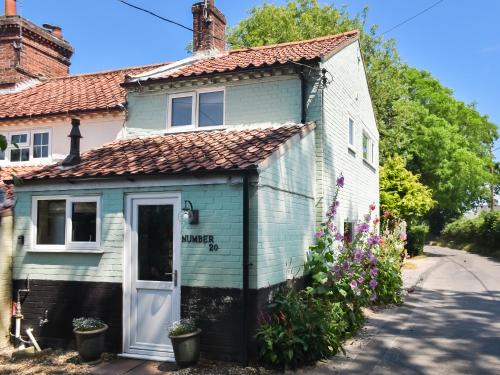 a small blue house with a white door and flowers at The Green One On The End in Thurton