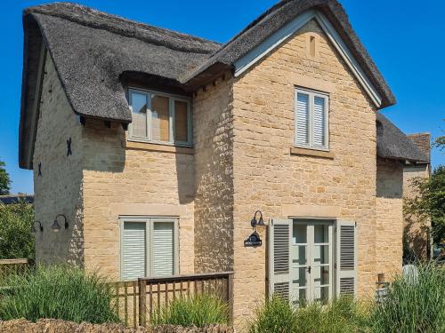 an old stone house with a thatched roof at Moorhens Cottage in Somerford Keynes