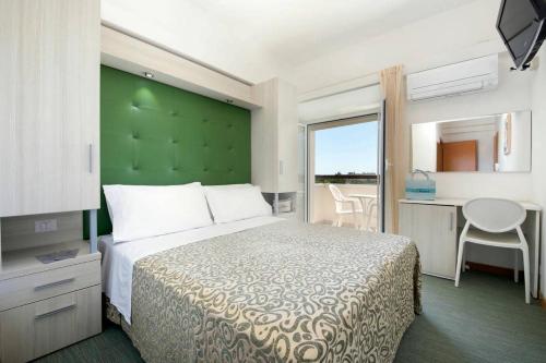 a bedroom with a bed with a green headboard and a table at Hotel Bassetti in Cervia