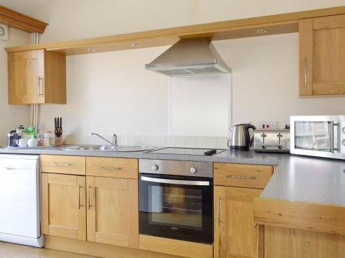 a kitchen with wooden cabinets and a stove top oven at Meadow View - Iom in Brandesburton