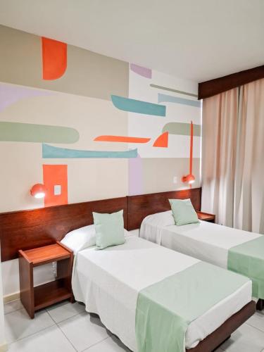 two beds in a room with colorful paintings on the wall at Alice Vitoria Hotel Arte by Nobile in Vitória