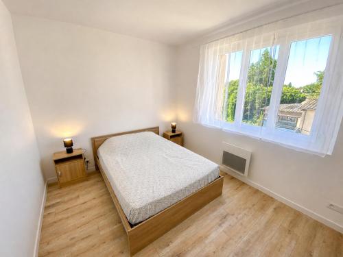a white bedroom with a bed and two windows at La Maison du Clain in Jaunay-Clan