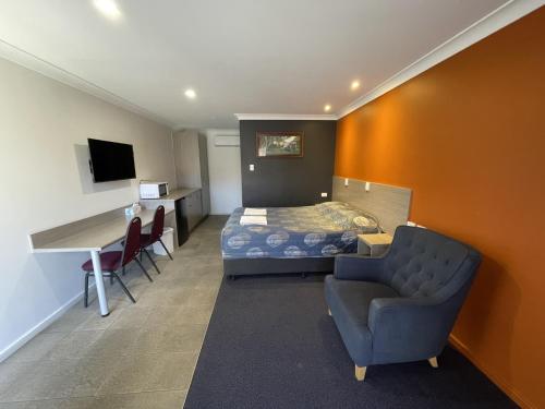 a hotel room with a bed and a chair and a desk at Homestead Motel in Dubbo