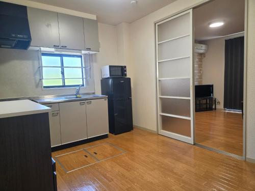 a kitchen with a black refrigerator and a room with wooden floors at アパートメントホテル憩 in Yanagawa