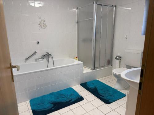 a bathroom with a tub and a toilet and blue rugs at Wohnen am Rande des Schwarzwaldes in Eggingen