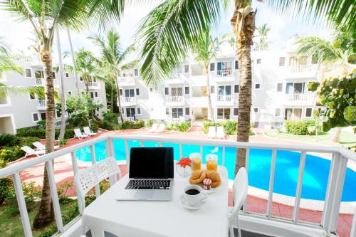 a table with a laptop on a balcony with a pool at SERENITY DEL CARIBE - LOS CORALES beach in Punta Cana