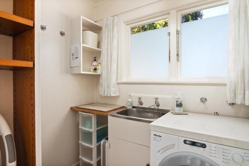 a small kitchen with a sink and a washing machine at Beachfront Kiwi bach with direct beach access in Gisborne
