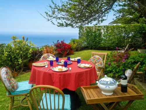 a table with a red tablecloth and chairs and the ocean at Sea-view house in Fajã da Ovelha with garden and terrace in Fajã da Ovelha