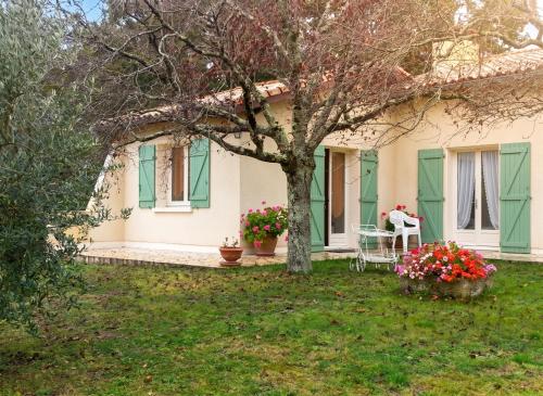 a house with green shutters and a tree and flowers at Appartement avec piscine à Montpezat-de-Quercy 40 m² in Montpezat-de-Quercy