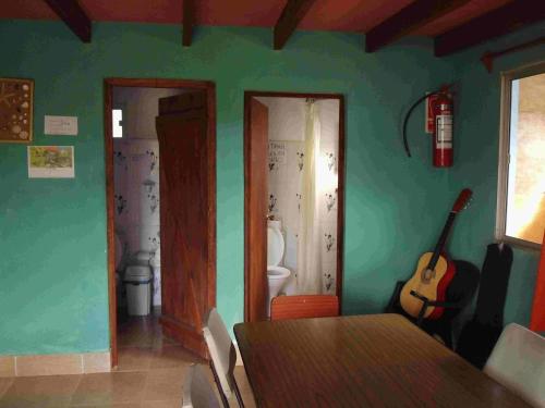 a room with a table and a bathroom with a guitar at Hostel Lo de Milton in Barra de Valizas