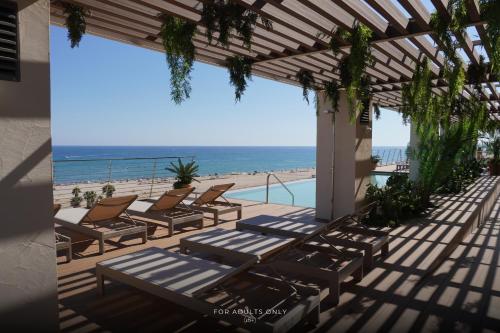 a patio with chairs and a pool and the ocean at Hotel Brisamar Suites in Comarruga