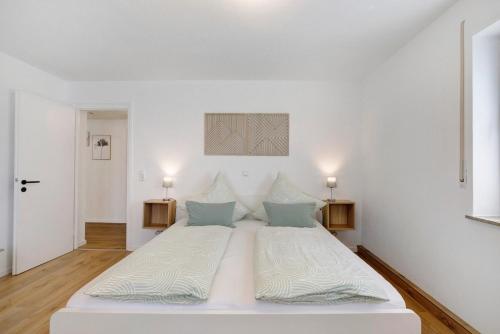 a white bedroom with a large white bed with blue pillows at Ferienwohnung am Alenberg in Münsingen