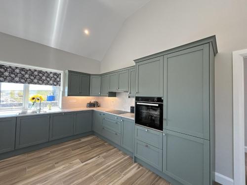 an empty kitchen with blue cabinets and a window at Ballyconneely Lodge in Ballyconneely