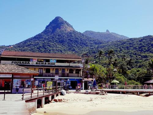 a building on the beach with a mountain in the background at Beira Mar Hostel & Suítes in Abraão