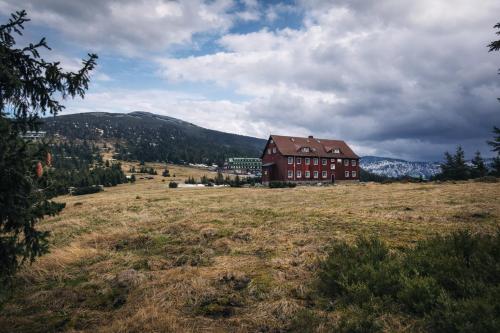 a large brown building in a field with a mountain at Hotel Spindlerova Bouda in Špindlerův Mlýn