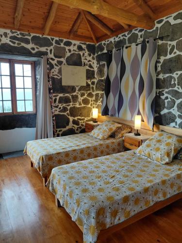 a bedroom with two beds and a stone wall at Casa do Bernardo in Feiteira