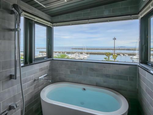 a bath tub in a bathroom with a large window at Atami Hotel Nagisakan in Atami