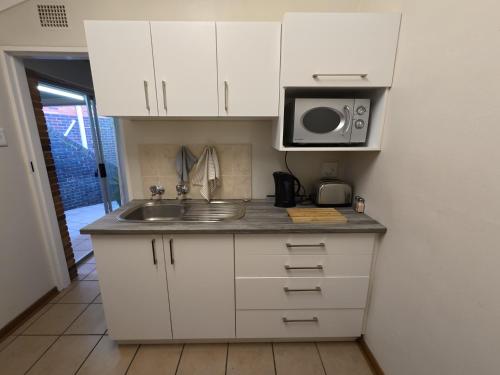 a kitchen with white cabinets and a sink and a microwave at Glendale Cottage in Bloemfontein