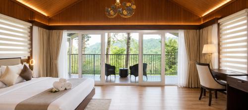 a bedroom with a bed and a desk and a balcony at Silent Brook Resort - Coorg in Madikeri