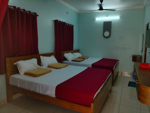 two beds in a room with red curtains at Malar Residency in Tirunallār