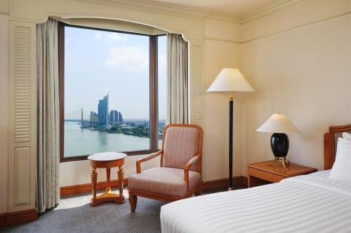 a hotel room with a bed and a chair and a window at Montien Riverside Hotel Bangkok in Bangkok