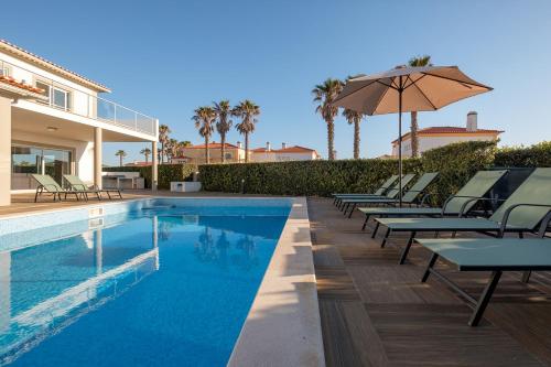 a swimming pool with chairs and an umbrella next to a house at Marvellous Villa in Óbidos