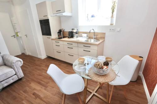 a small kitchen with a glass table and white chairs at Le Corail - centre-ville - TV in Pontivy