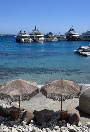 two straw umbrellas on a beach with boats in the water at Beachfront Mykonos Guest House in Ornos