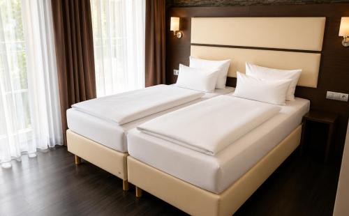 two white beds in a room with windows at DORMERO Hotel Werther in Werther