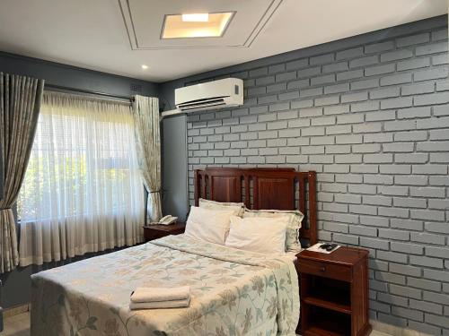 a bedroom with a bed and a brick wall at Nduna Legacy Lodge in Harare