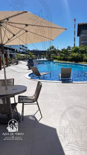a pool with chairs and a table and an umbrella at Refúgio Azul de Porto in Porto De Galinhas