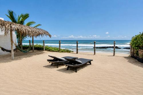 two benches on a beach with the ocean at Sandy Feet House in Puerto Villamil