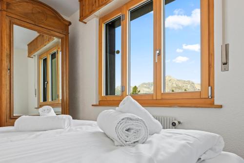 a bedroom with a bed with white sheets and windows at Logement spacieux et charmant in Nendaz