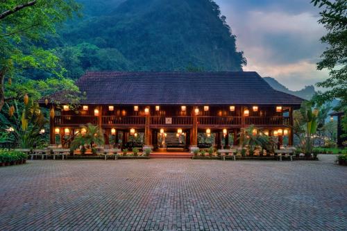 a large building with a mountain in the background at Ui Valley Resort in Ninh Binh